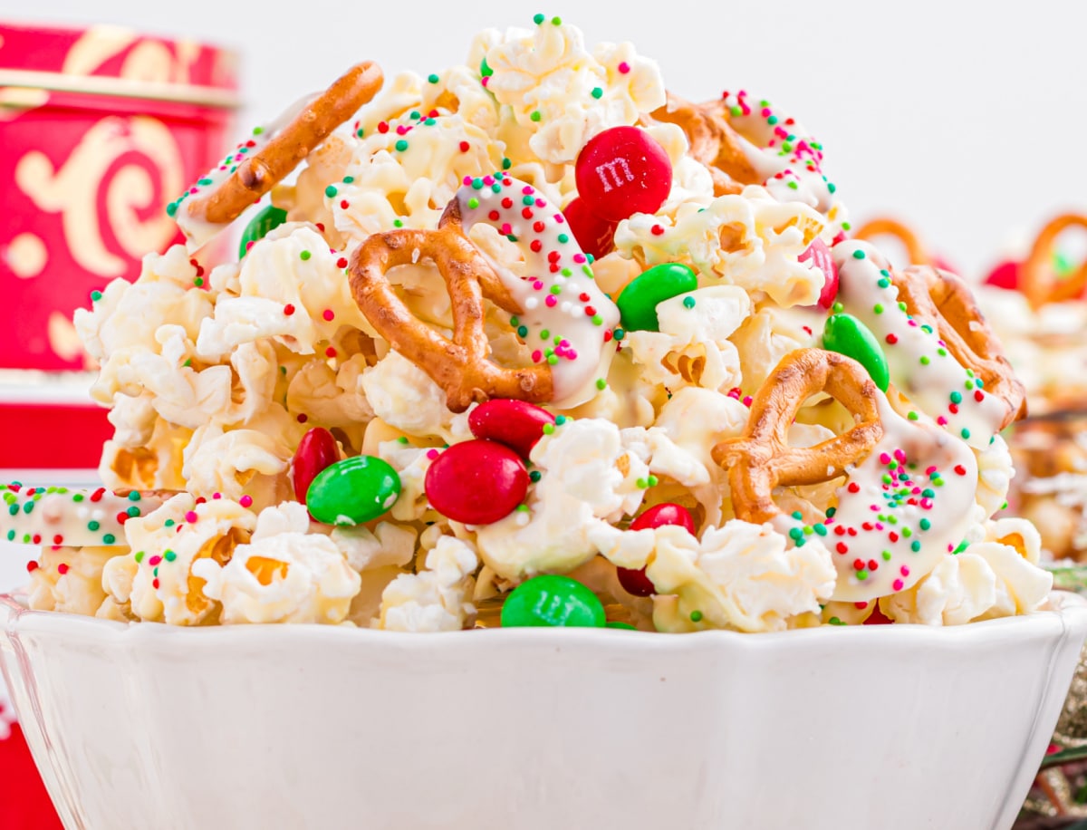Christmas Popcorn Mix in a white bowl ready to eat. christmas popcorn mix in a white bowl revealing M&m's