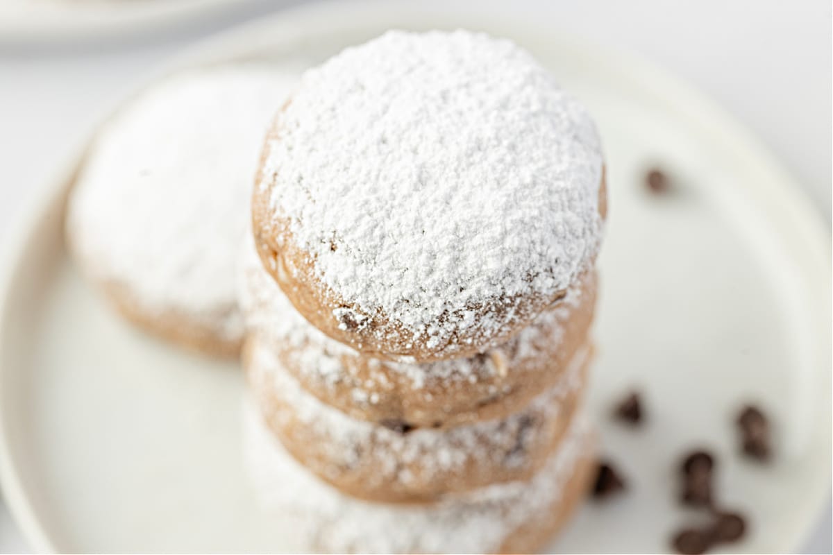 A stack of powdered cookies on a plate. A stack of soft, sugar-dusted cookies showing their tender texture.
