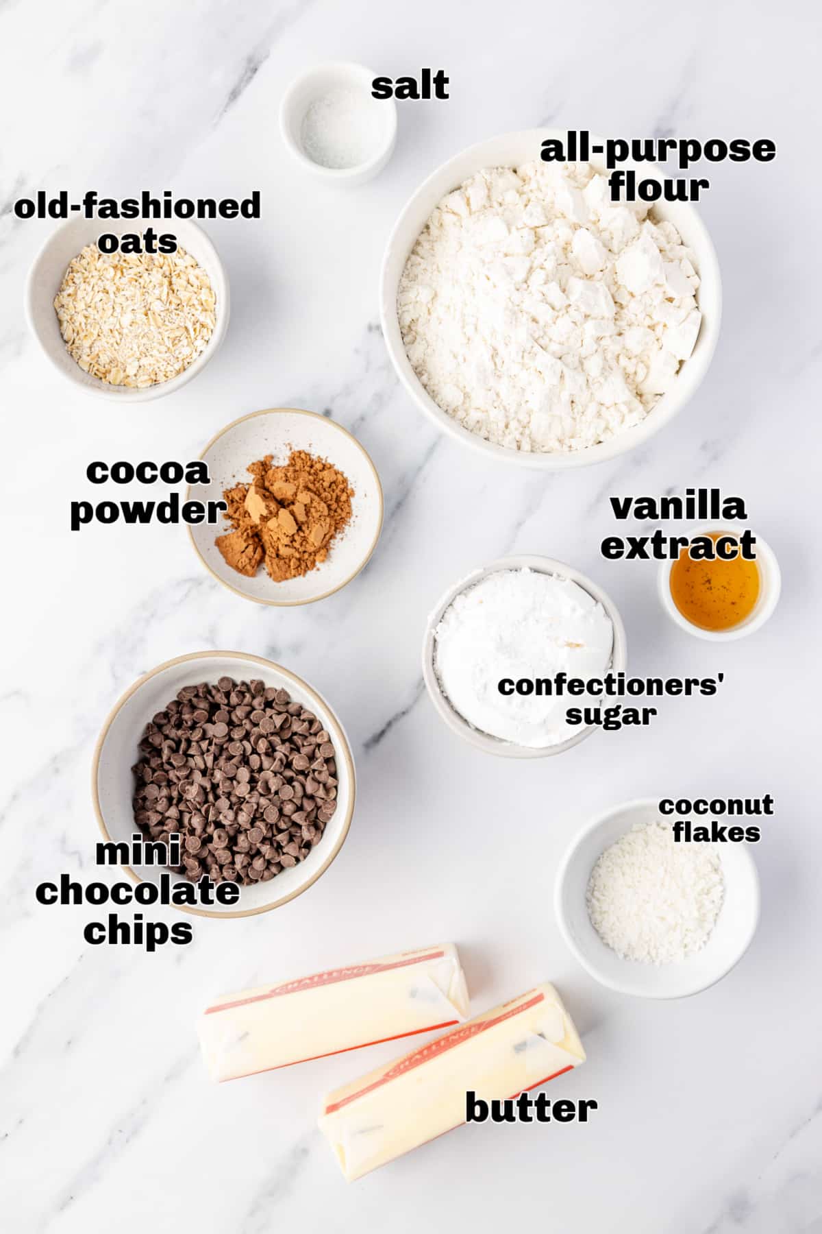 Ingredients laid out before mixing the cookie dough. Danish wedding cookies Measured ingredients arranged on a marble surface, including flour, oats, cocoa powder, chocolate chips, butter, and confectioners’ sugar.