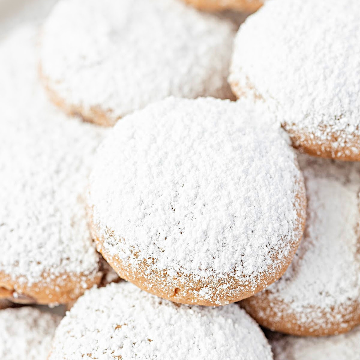 A plate of Danish wedding cookies covered in a thick layer of confectioners’ sugar, arranged closely so their wintery coating fills the frame.
