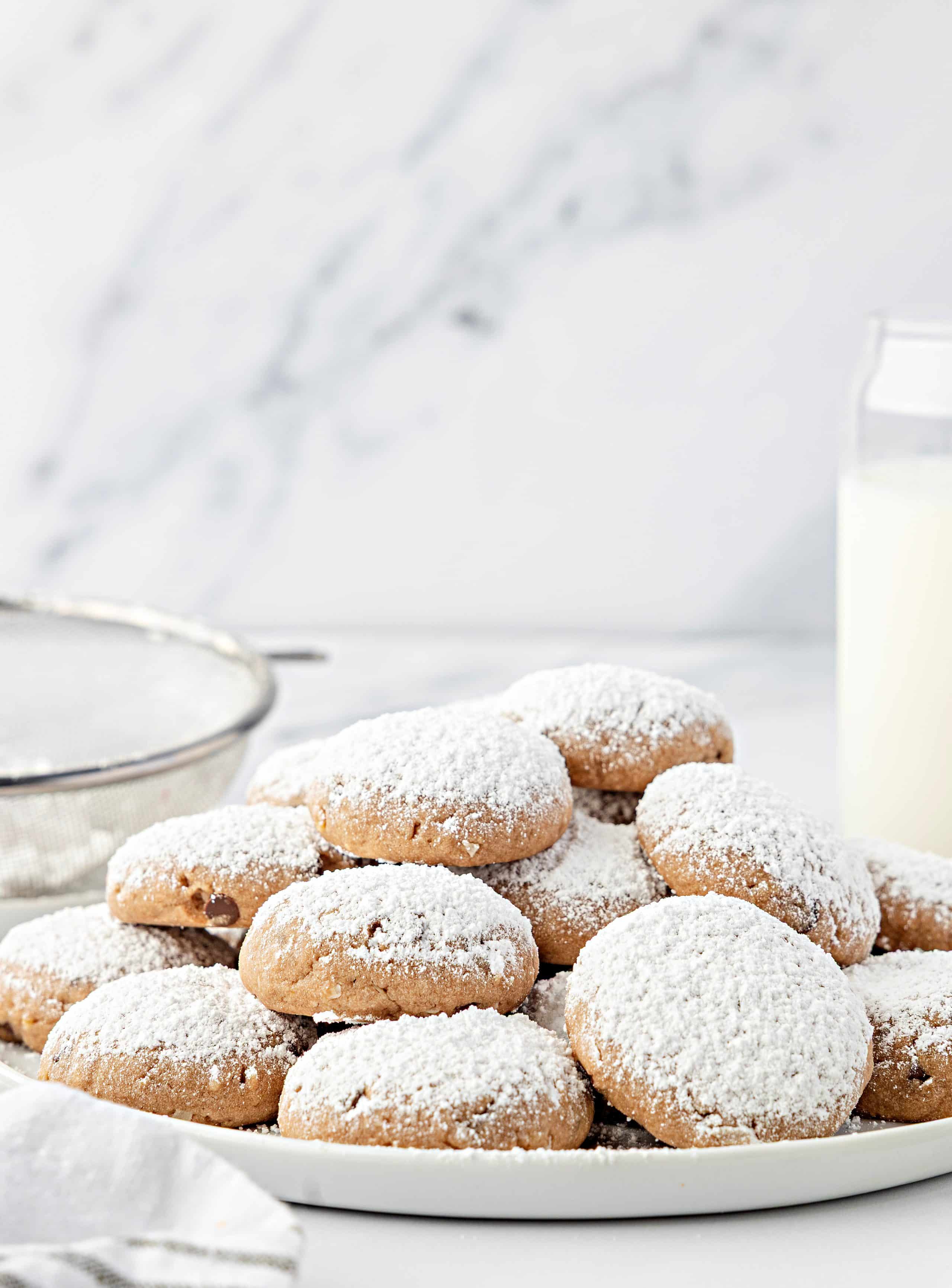 Cookies arranged on a plate beside a cooling rack and milk. An overhead view of soft Danish meltaway cookies on a plate with a thick layer of confectioners’ sugar.