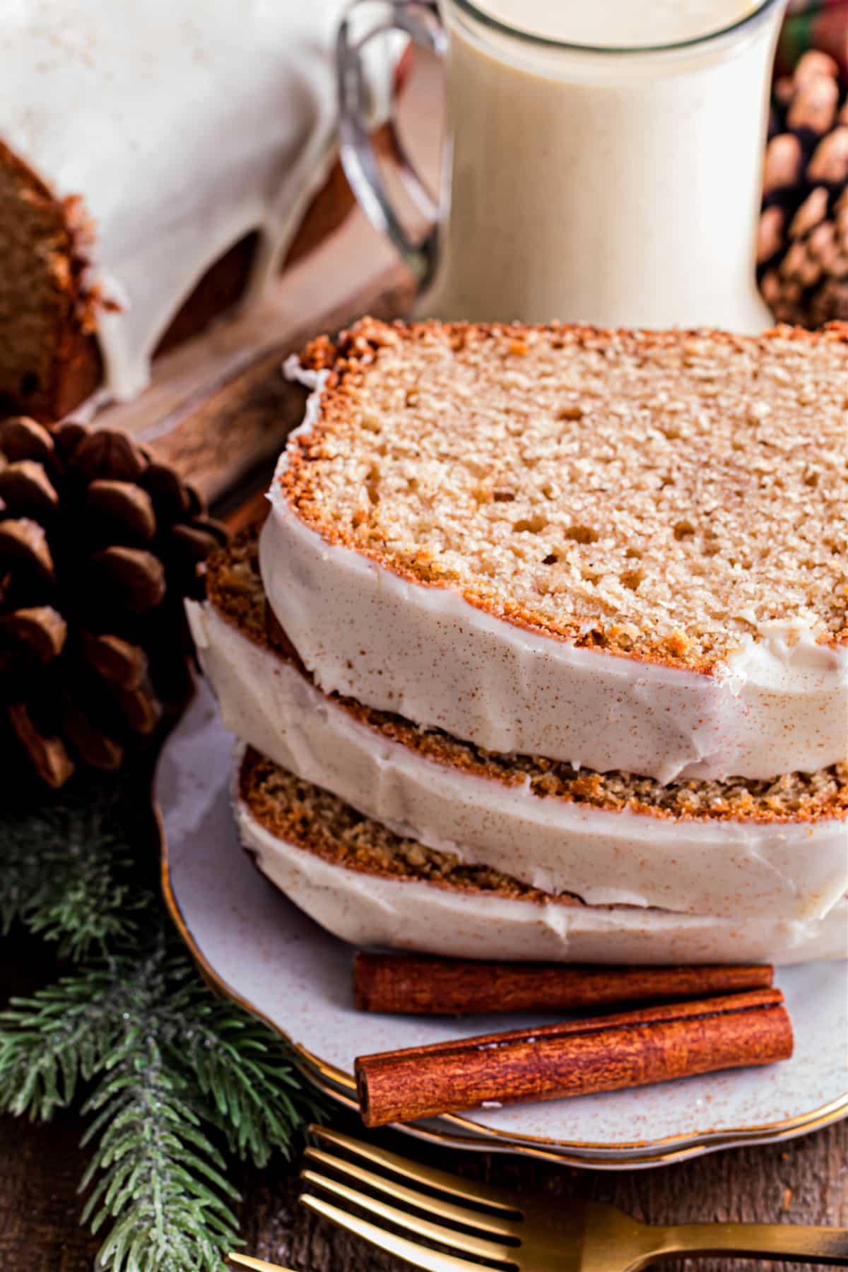 Sliced holiday eggnog loaf with glaze and warm spices Sliced eggnog loaf with a set eggnog glaze, showing a tender crumb and spiced interior, stacked on a plate with cinnamon sticks nearby.