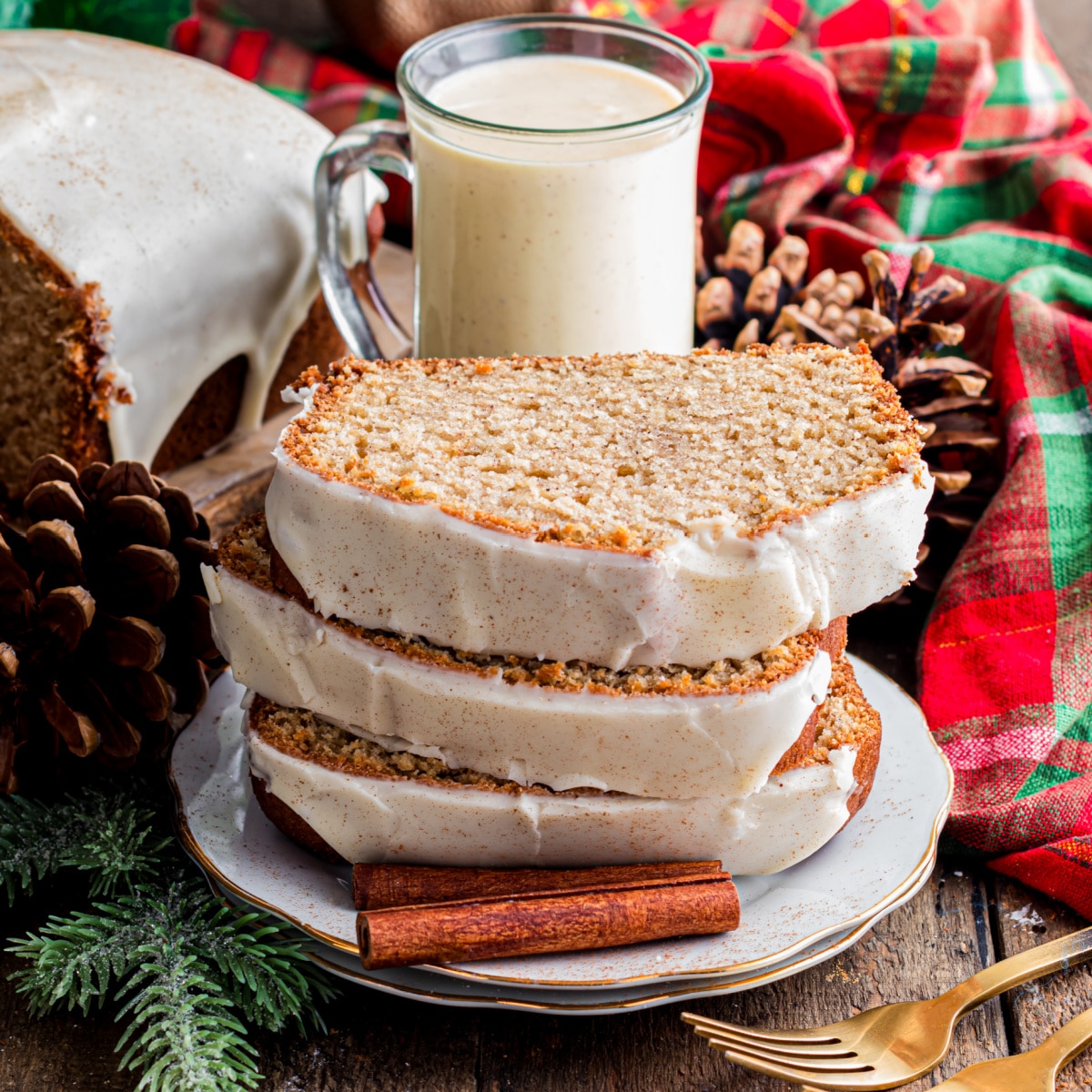 Eggnog quick bread sliced and glazed on a wooden board with cinnamon sticks and holiday accents.
