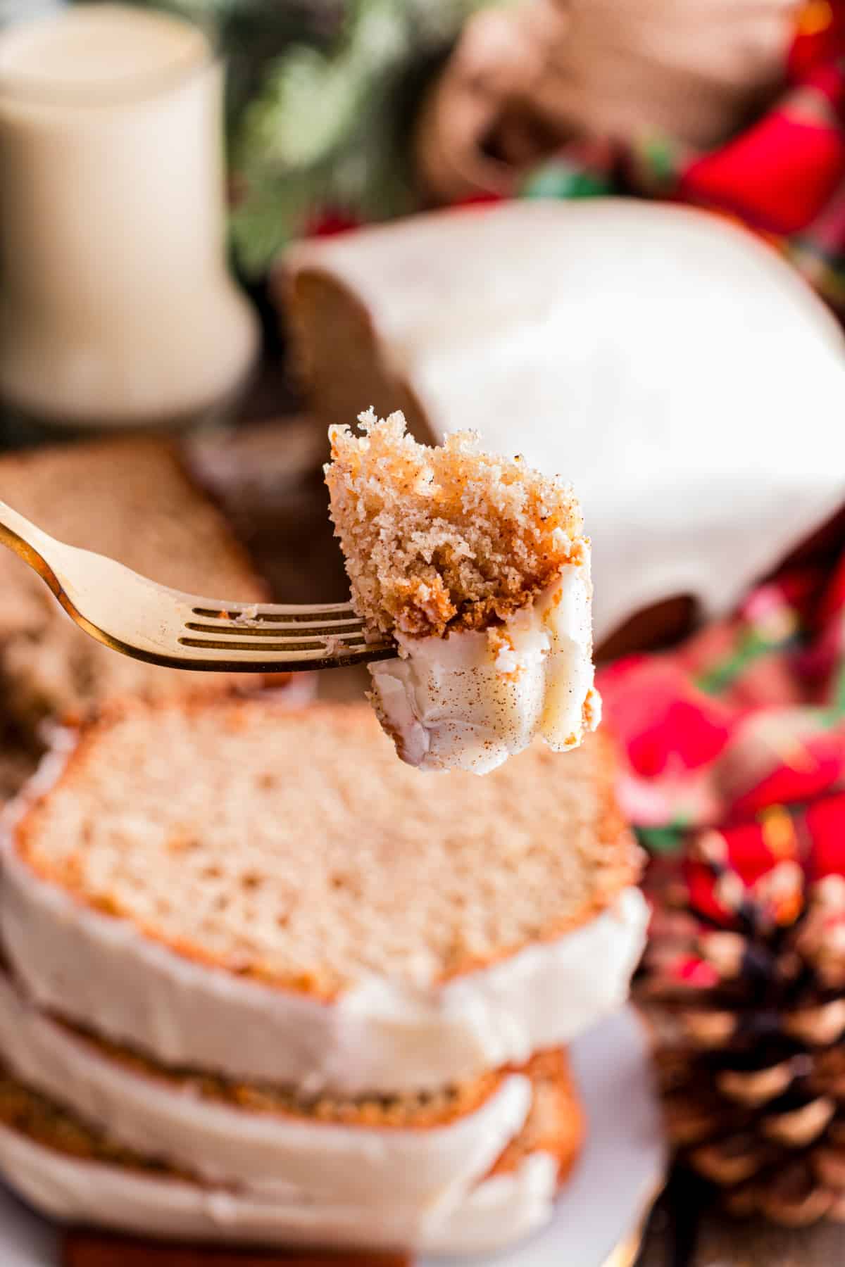 Eggnog bread with glaze and tender holiday crumb Fork holding a bite of eggnog bread with a soft, spiced crumb and set eggnog glaze, with the loaf blurred in the background on a holiday table.