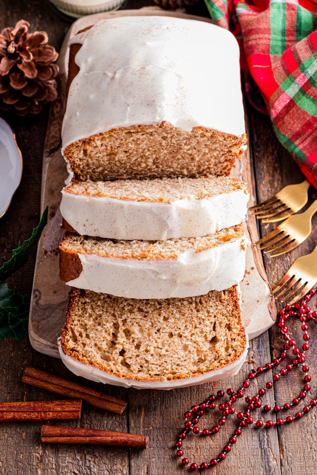 Eggnog bread with set glaze and spiced crust Close-up of eggnog bread with a smooth eggnog glaze dripping over the edge, resting on a wooden board with cinnamon sticks and holiday accents.