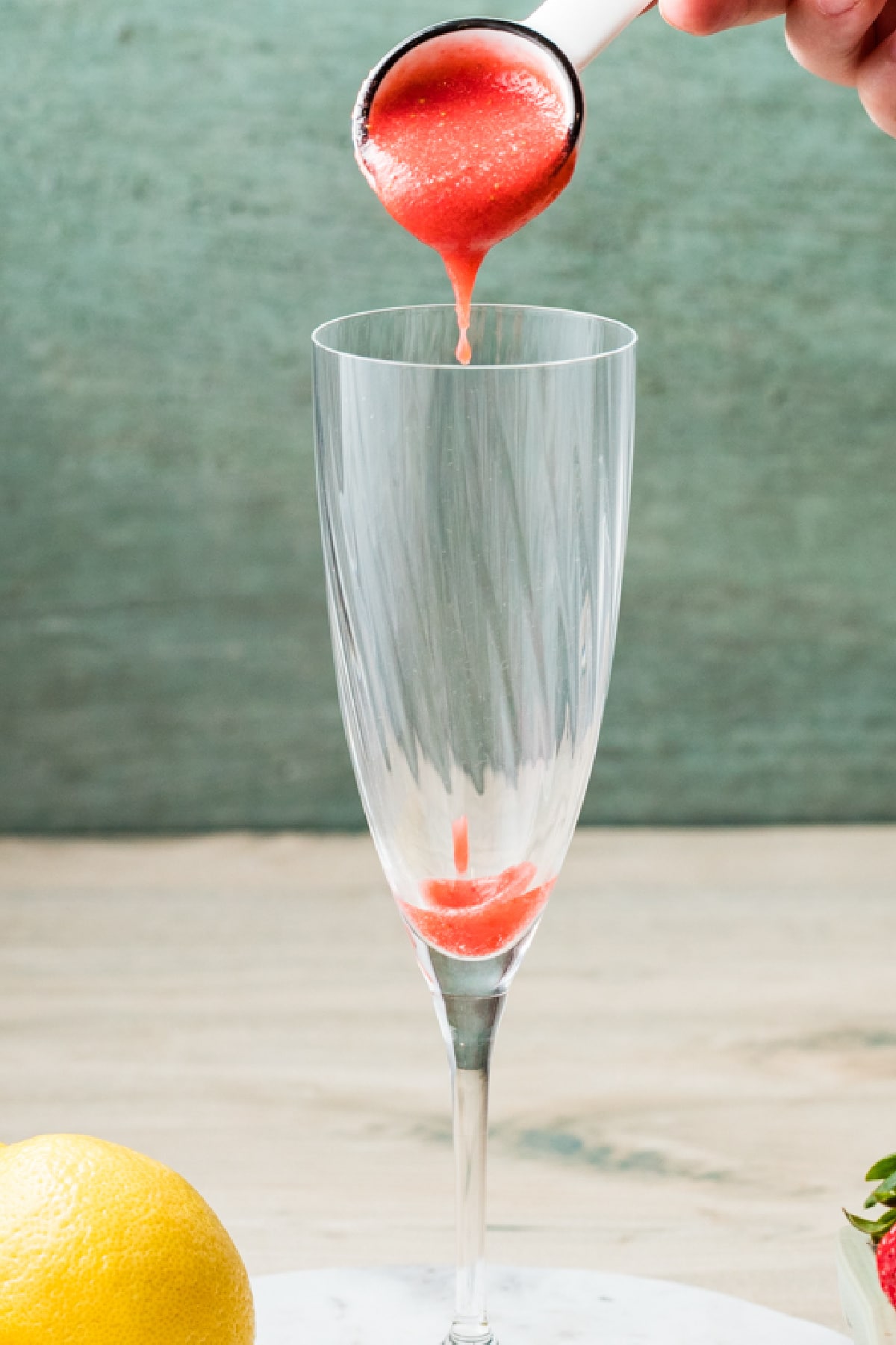 Strawberry purée being spooned into the bottom of a champagne flute.