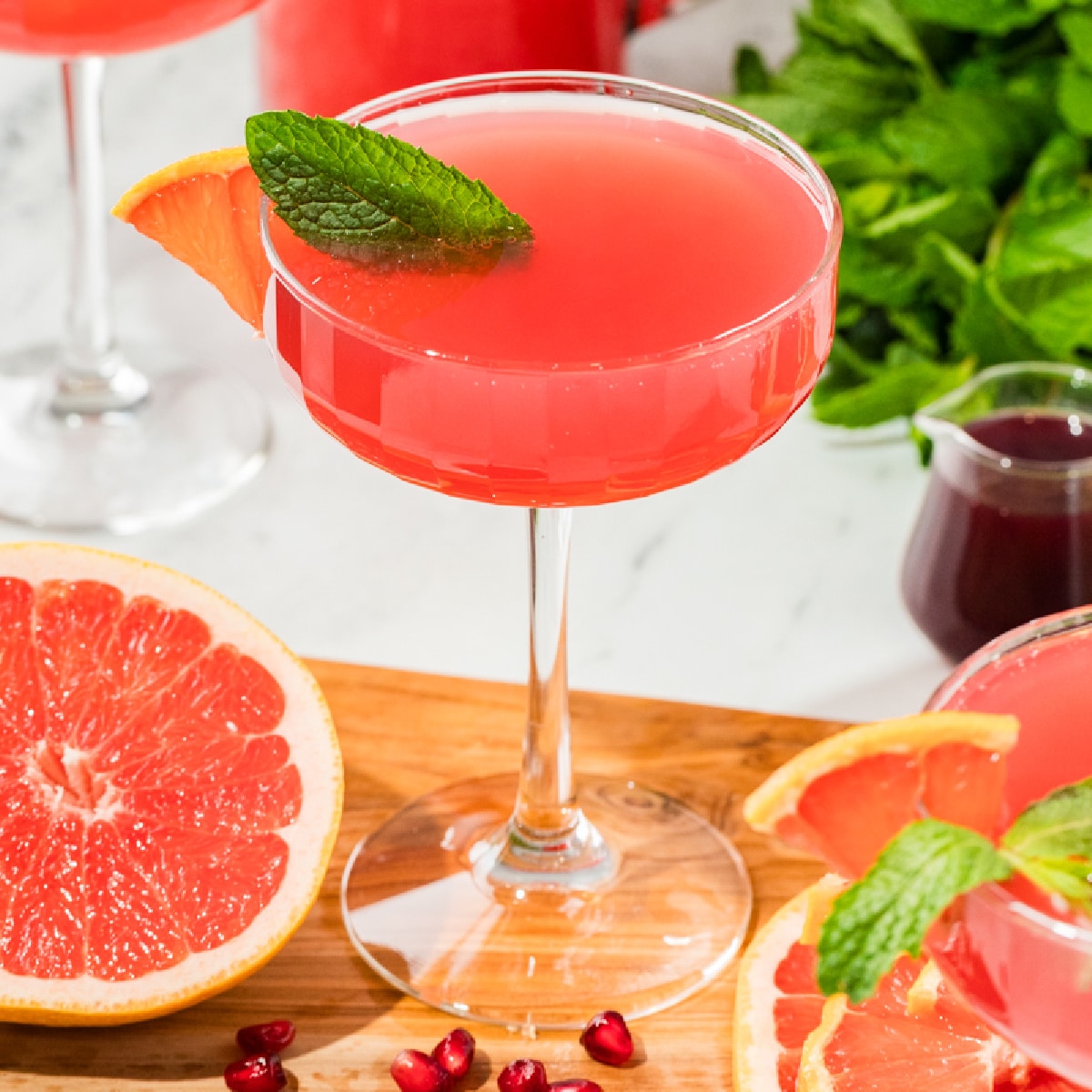 Grapefruit pomegranate gin fizz in a coupe glass, topped with prosecco and garnished with grapefruit and mint for a holiday brunch cocktail.