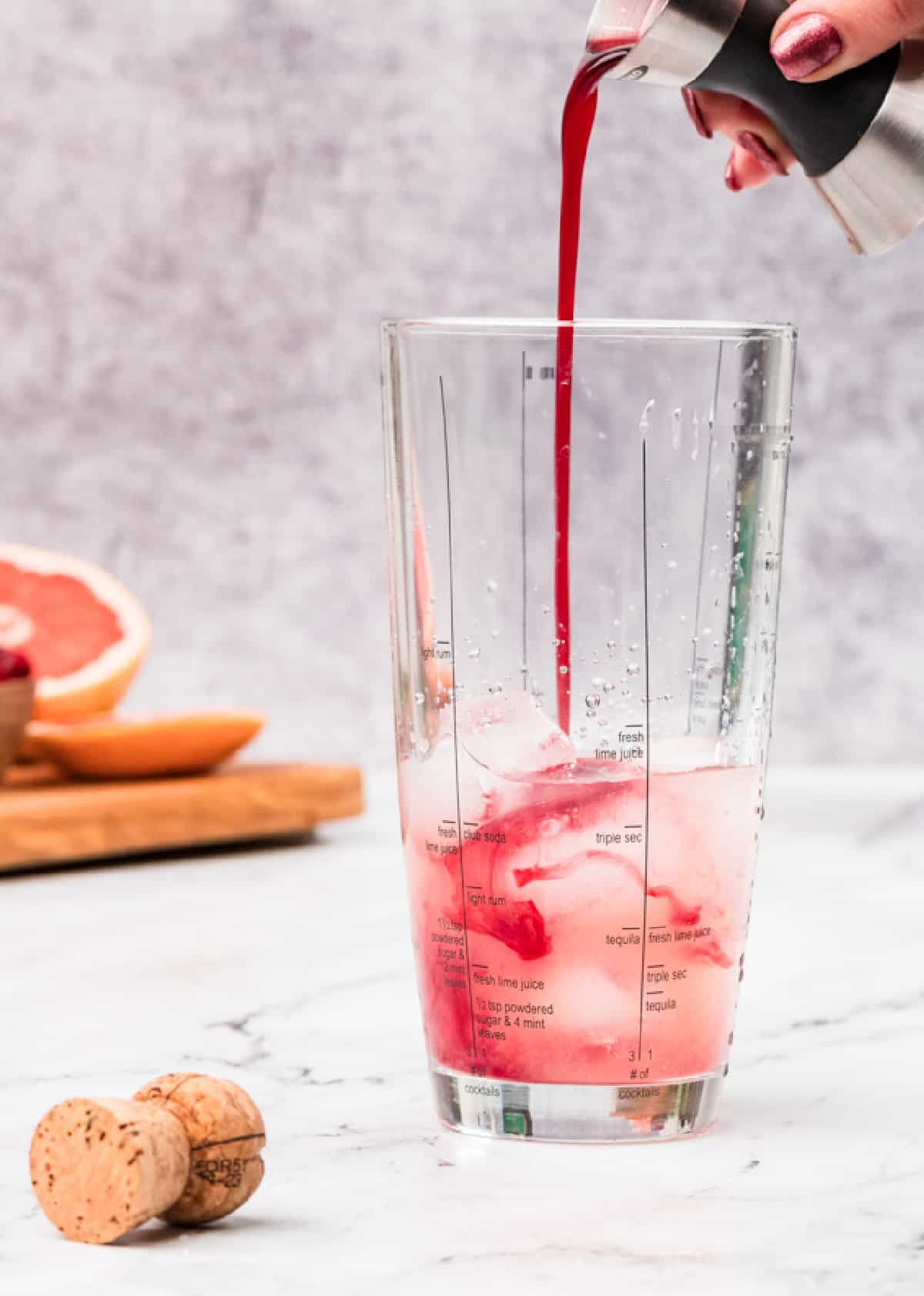 Pomegranate simple syrup poured into a cocktail shaker with ice and grapefruit juice. Pomegranate simple syrup being poured into a cocktail shaker filled with ice and grapefruit juice, showing the deep red color as it blends.