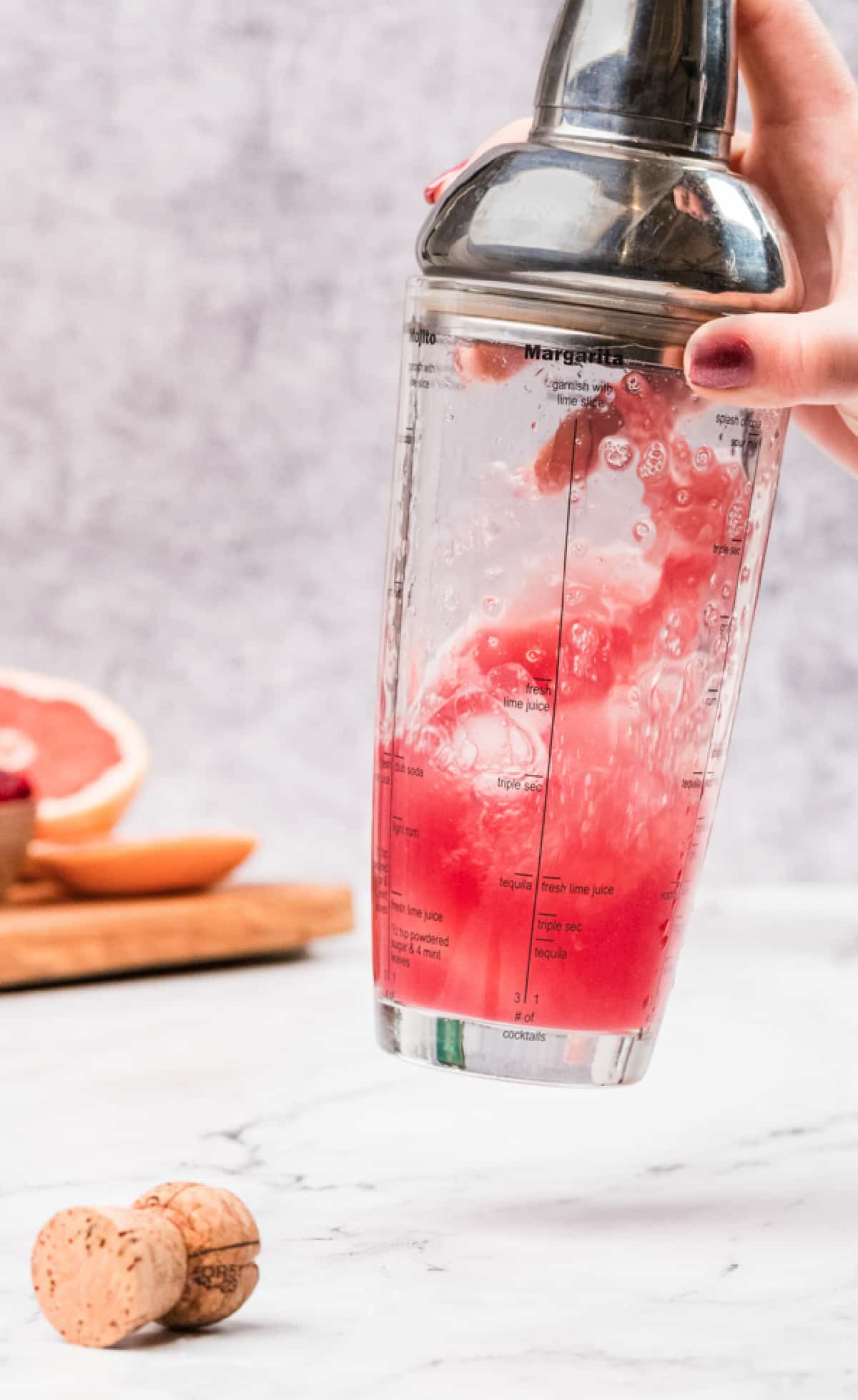 Shaking a grapefruit and pomegranate gin cocktail with ice in a cocktail shaker. A cocktail shaker being shaken with ice, grapefruit juice, gin, and pomegranate syrup, showing the pink mixture swirling inside.