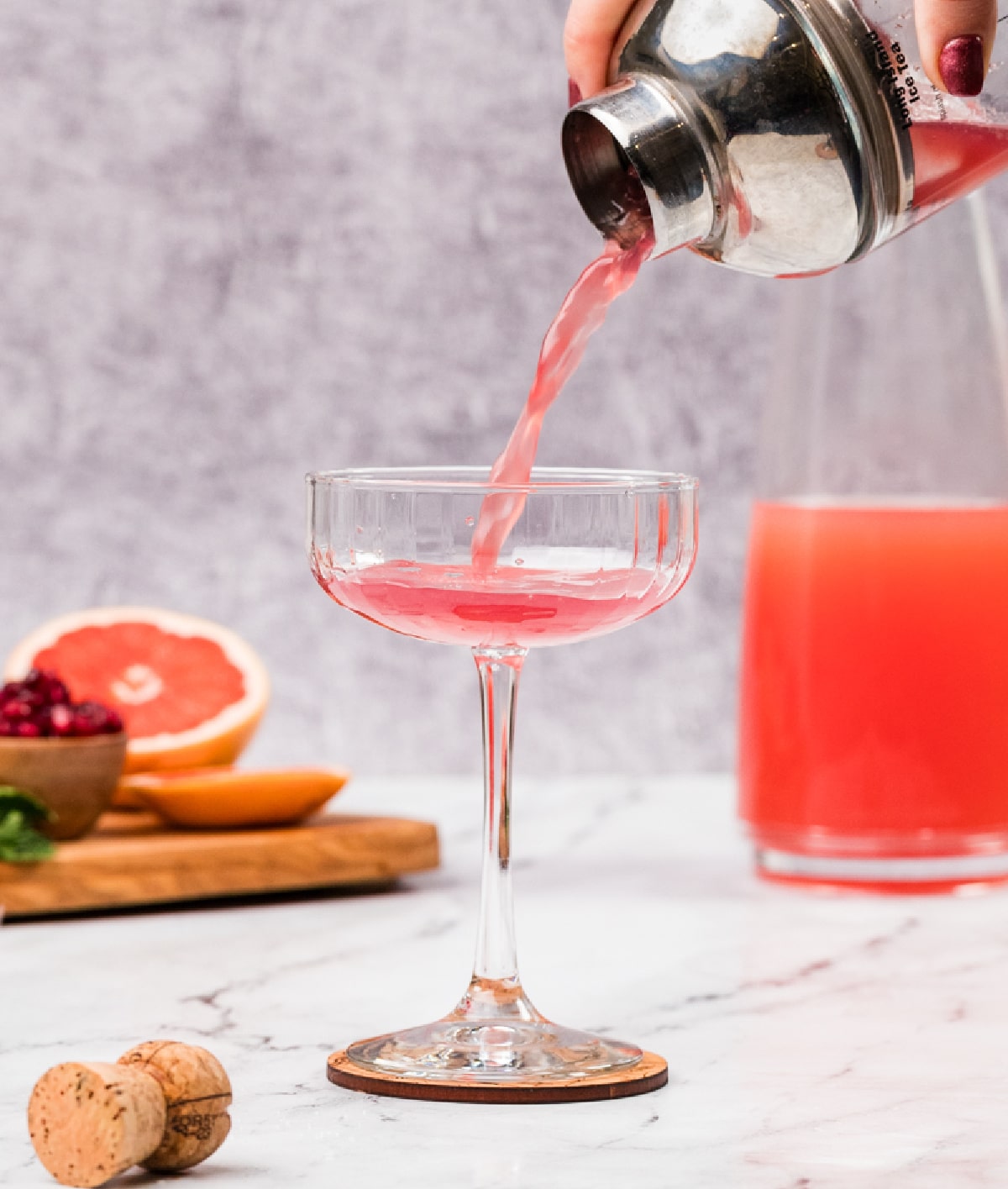 Straining a grapefruit and pomegranate cocktail into a coupe glass. Straining a pink grapefruit and pomegranate cocktail into a coupe glass, showing the clear pour and pale rosy color before adding prosecco.