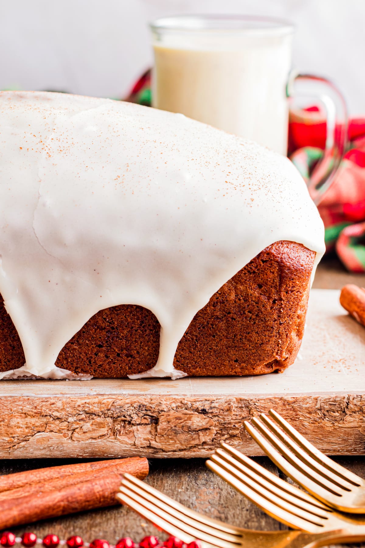 Eggnog bread sliced with set glaze and warm spices Sliced eggnog bread with a thick eggnog glaze, showing a soft crumb and lightly spiced interior on a wooden board with holiday accents.