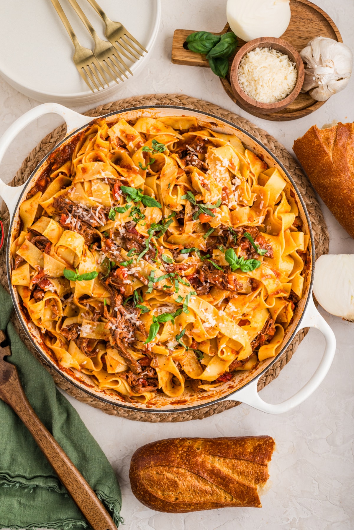 A large pot filled with tender shredded beef ragù and wide pappardelle noodles, topped with fresh basil and parmesan, ready to serve with bread.