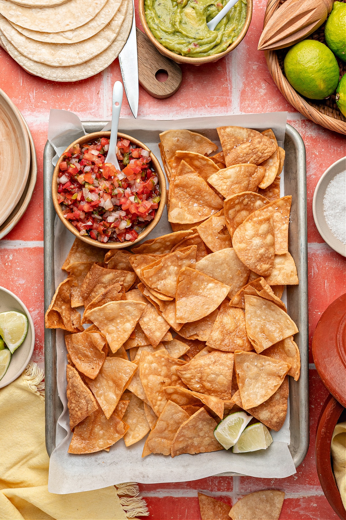 A sheet pan piled with homemade tortilla chips, golden and blistered, ready for dipping.