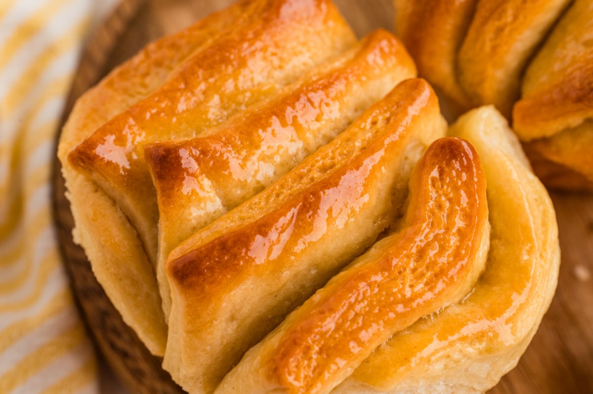 A tight close-up showing the shiny honey butter glaze soaking into the folded layers of a freshly baked roll. Close view of a golden pull-apart roll with glossy honey butter coating the folded layers.