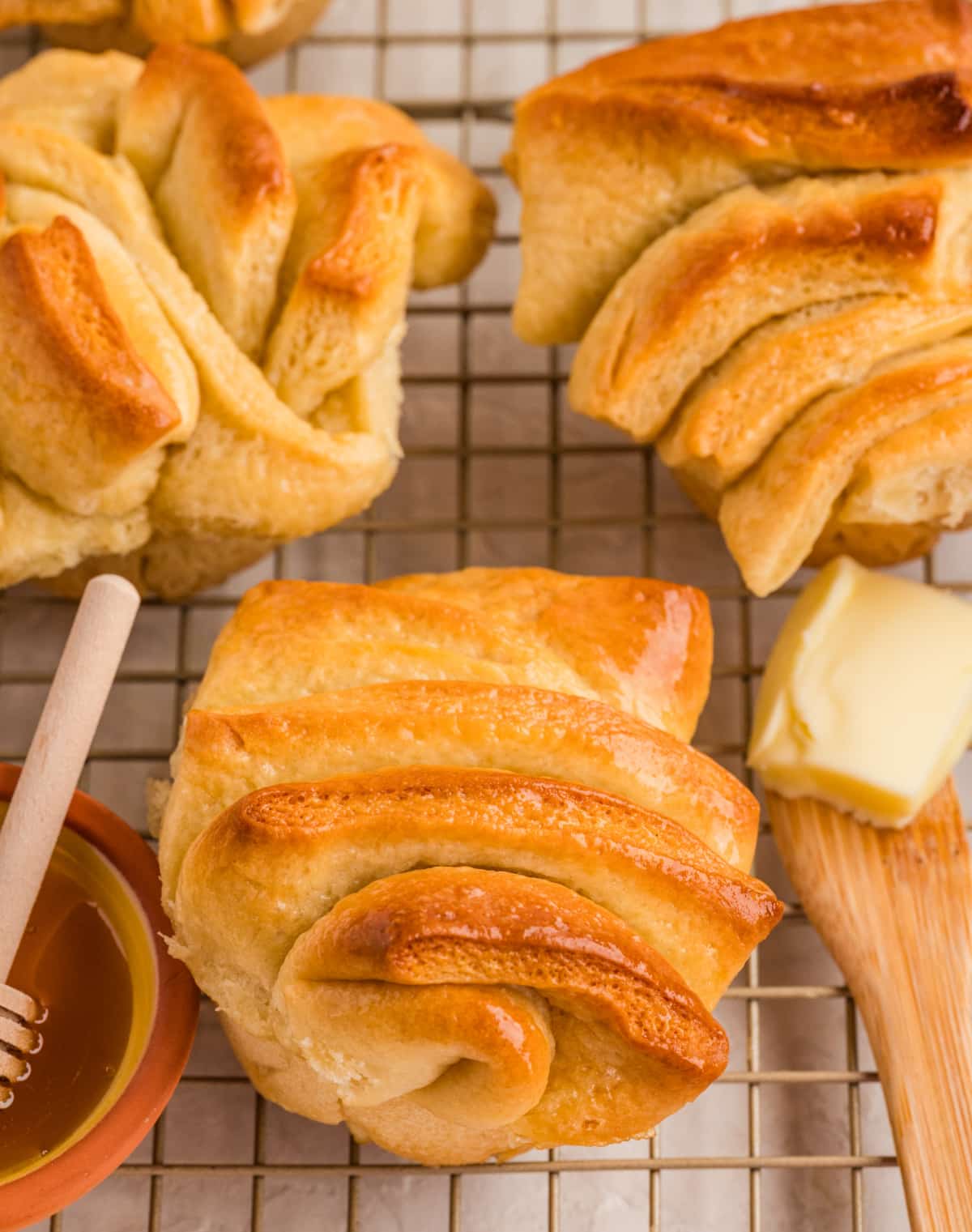 Honey butter pull-apart rolls resting on a cooling rack, finished with a light honey butter glaze and deeply golden layers. Honey butter pull-apart rolls cooling on a wire rack with glossy tops and soft folded layers.