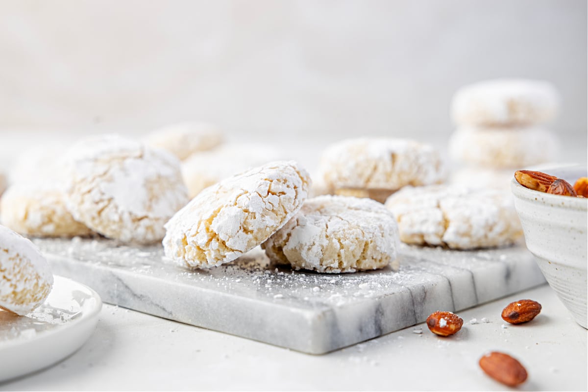 Powdered almond cookies with a soft, crackled finish arranged on a marble board in bright winter light.