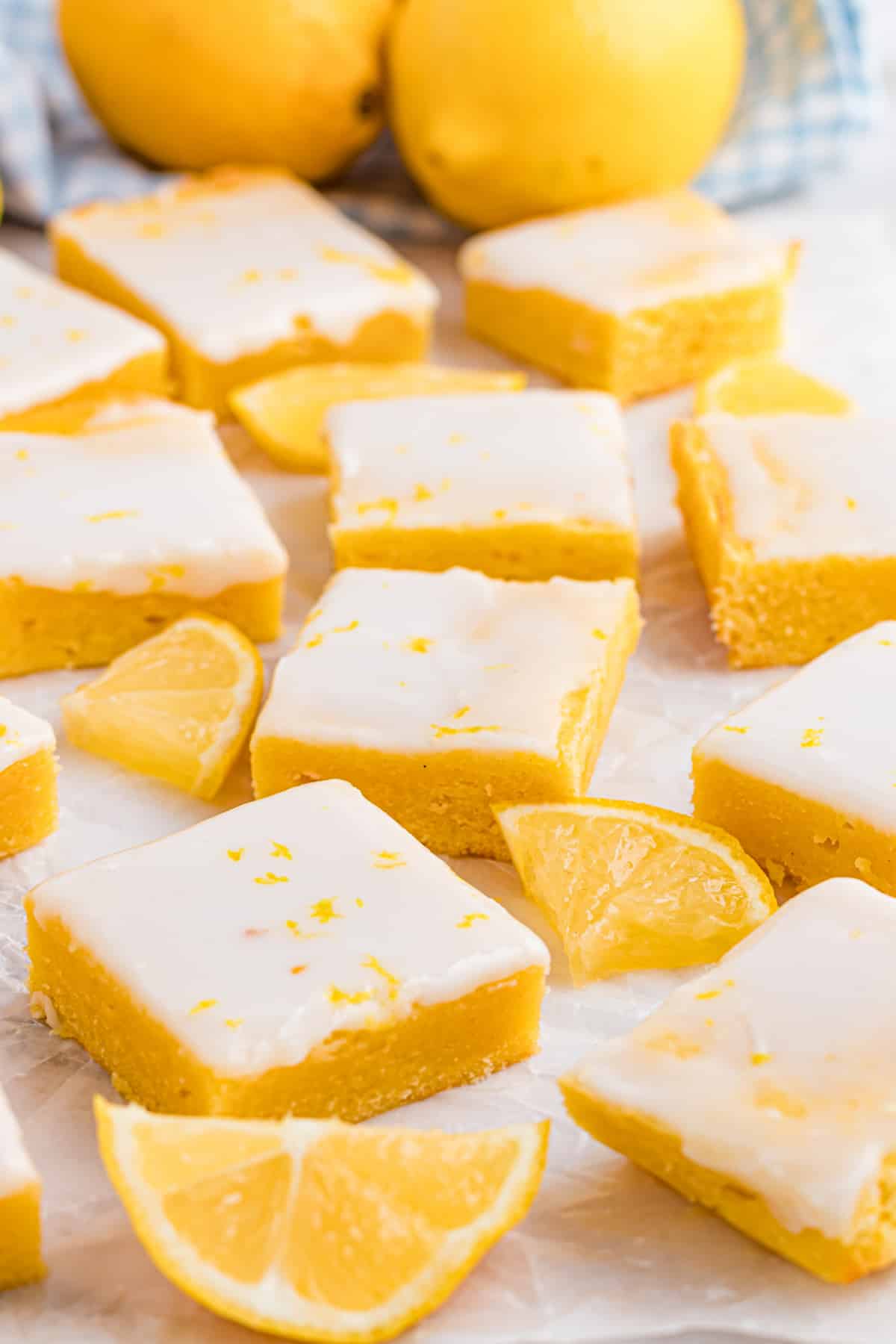 Buttery lemon blondies with fresh lemon glaze sliced into even squares, photographed on parchment with lemon wedges nearby. Lemon blondies cut into neat squares with a thin lemon glaze, showing a soft, dense crumb and clean edges on parchment paper.