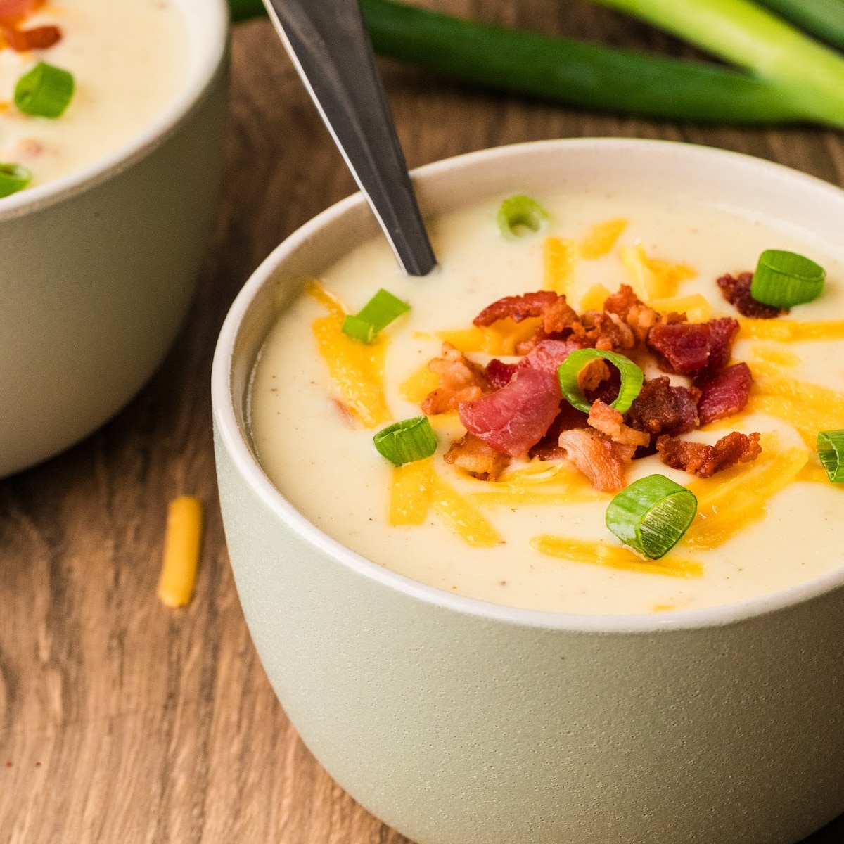 Loaded baked potato soup topped with bacon, cheddar, and scallions, served thick and creamy in a bowl.