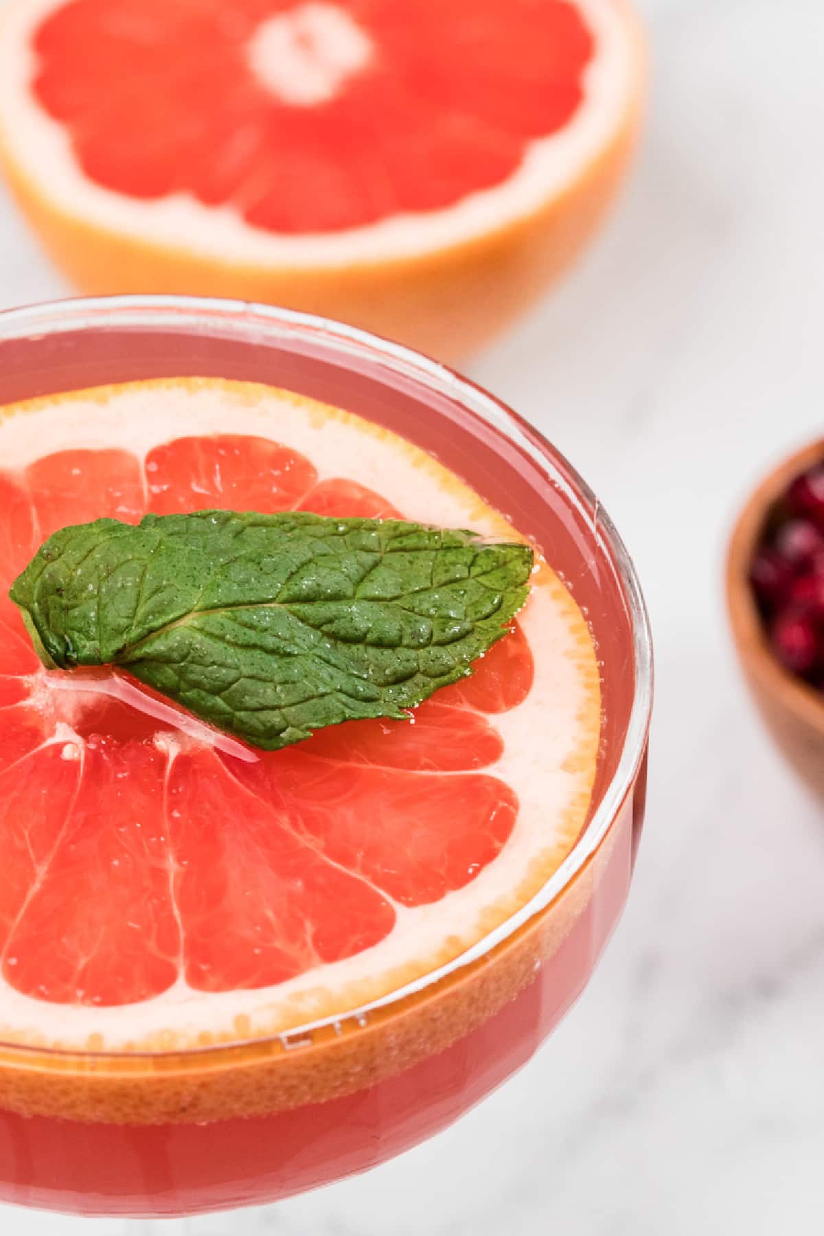 Close-up of a grapefruit and pomegranate cocktail with mint and citrus garnish. Close-up of a pink grapefruit and pomegranate cocktail garnished with a floating grapefruit slice and fresh mint, showing the clear rim and saturated winter color.