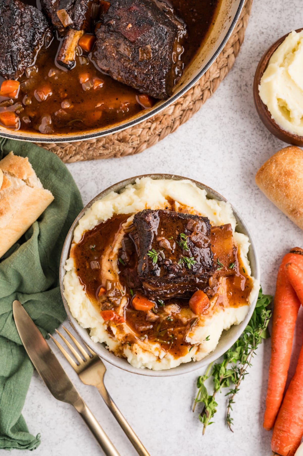 Bowl of braised beef short ribs over mashed potatoes with glossy sauce and tender vegetables. Braised beef short ribs served over mashed potatoes, finished with thick sauce, carrots, and fresh thyme on top.