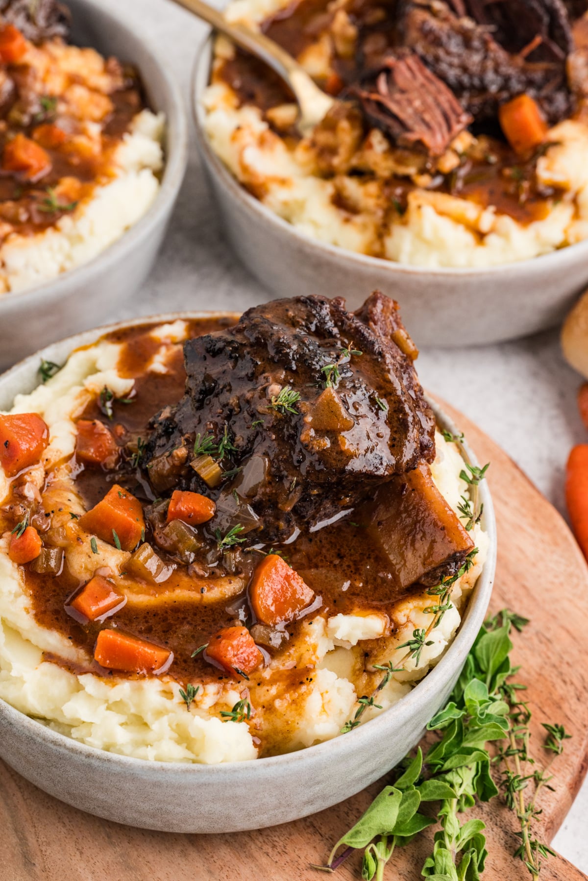 Oven-braised short ribs served over creamy mashed potatoes with a rich, savory sauce and tender vegetables. A bowl of oven-braised short ribs resting on mashed potatoes, spooned with glossy sauce and scattered with carrots and fresh herbs.