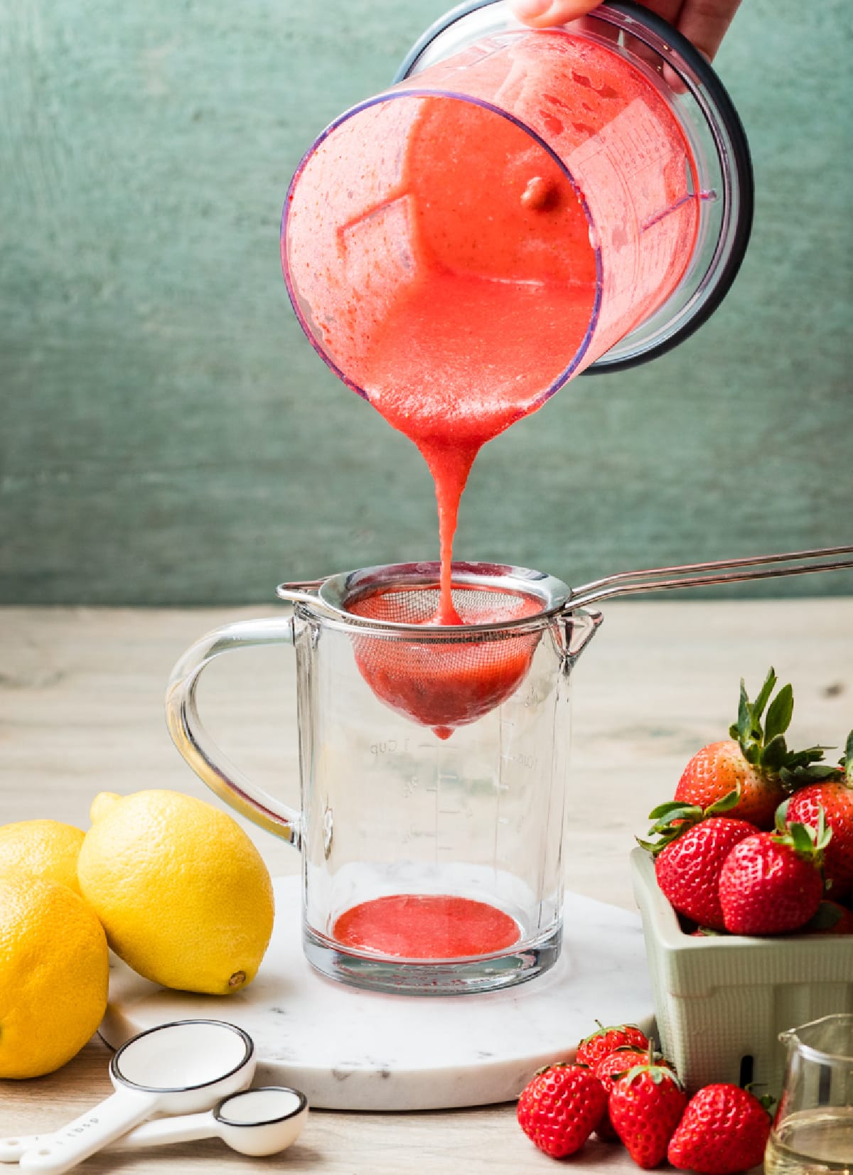Fresh strawberry purée being strained through a fine-mesh sieve into a glass measuring cup.