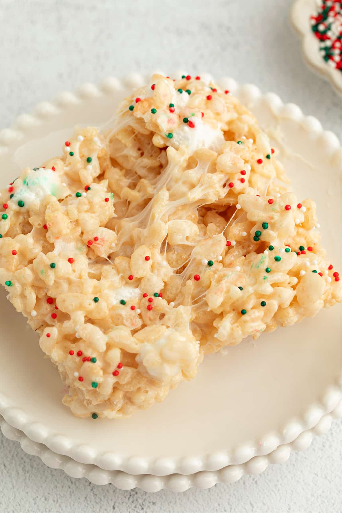 Christmas Sugar Cookie Rice Krispie Treats pulled apart on a plate to show gooey marshmallow stretch and festive holiday sprinkles.