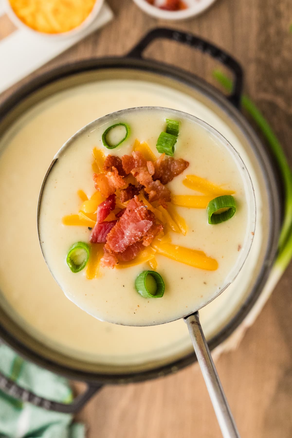 A ladle lifting thick loaded baked potato soup with bacon, cheddar, and scallions. A ladle of loaded baked potato soup showing its thick, creamy texture with bacon, melted cheddar, and scallions.