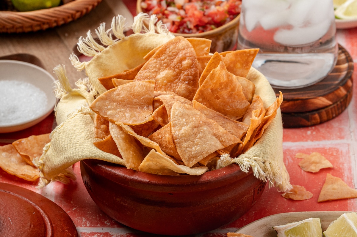 A rustic bowl lined with cloth and filled with easy fried tortilla chips, showing crisp edges and an even golden color ready for serving.