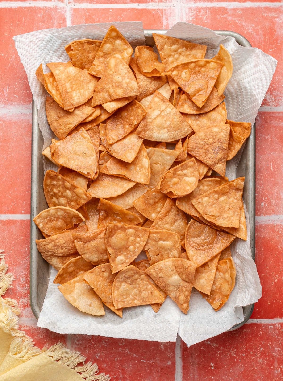 A pan of easy fried tortilla chips draining on paper towels, showing blistered surfaces and an even golden color after frying.