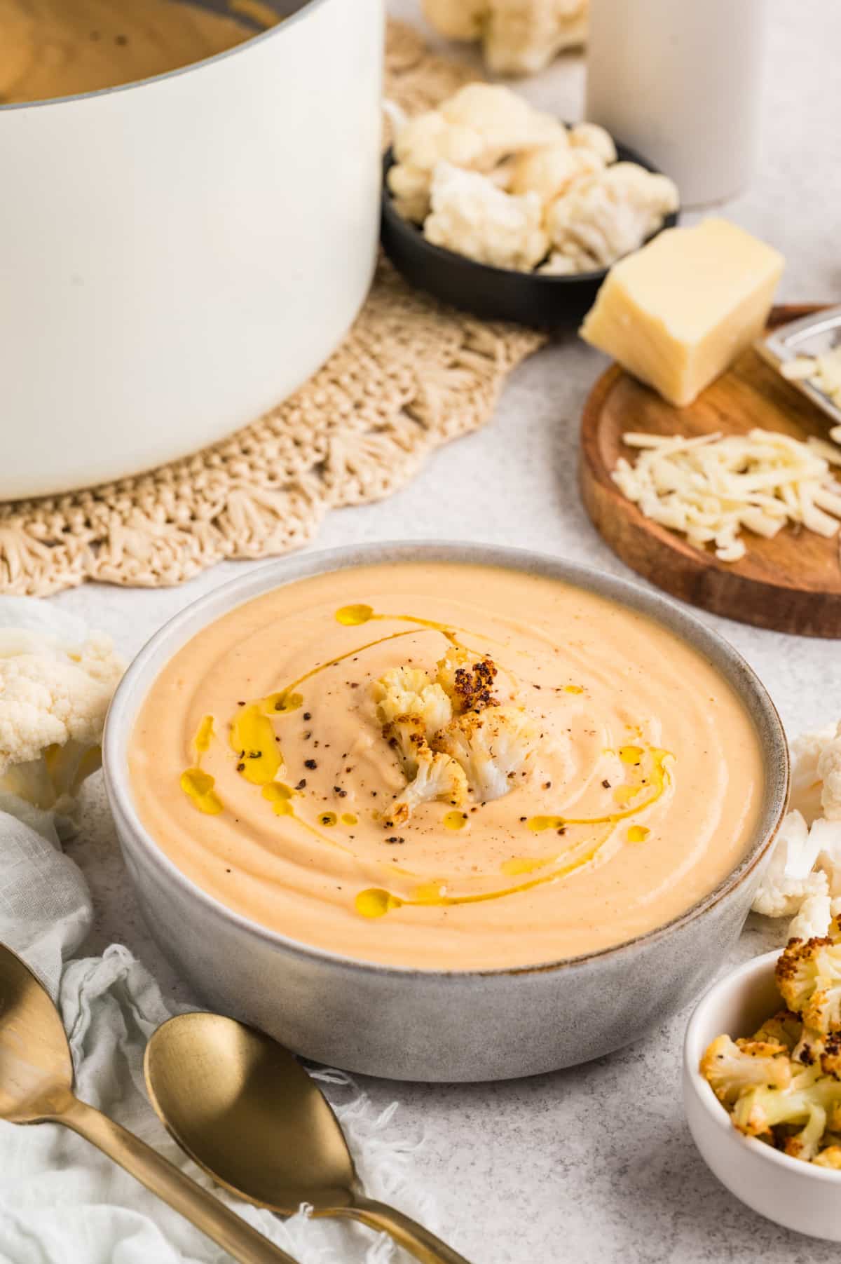 A finished bowl of Roasted Cauliflower Soup topped with roasted cauliflower florets and a drizzle of olive oil. Roasted Cauliflower Soup finished with olive oil, black pepper, and caramelized cauliflower florets in a shallow bowl.