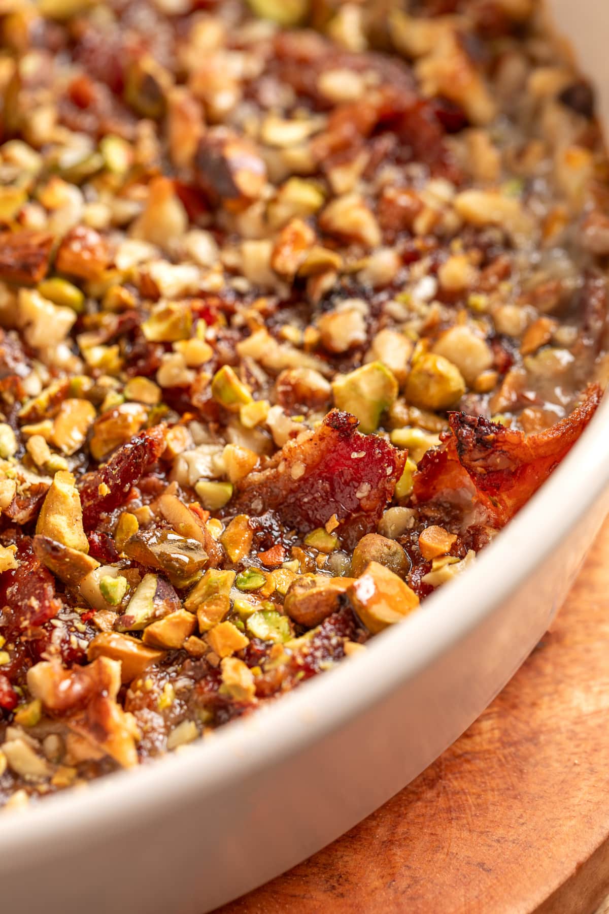 A close-up view of Boursin Bacon Pistachio & Fig Dip fresh from the oven with caramelized bacon, chopped nuts, and a glossy, bubbling surface. Close-up of Boursin Bacon Pistachio & Fig Dip showing crisp bacon, chopped pistachios, walnuts, and bubbling cheese at the edges.