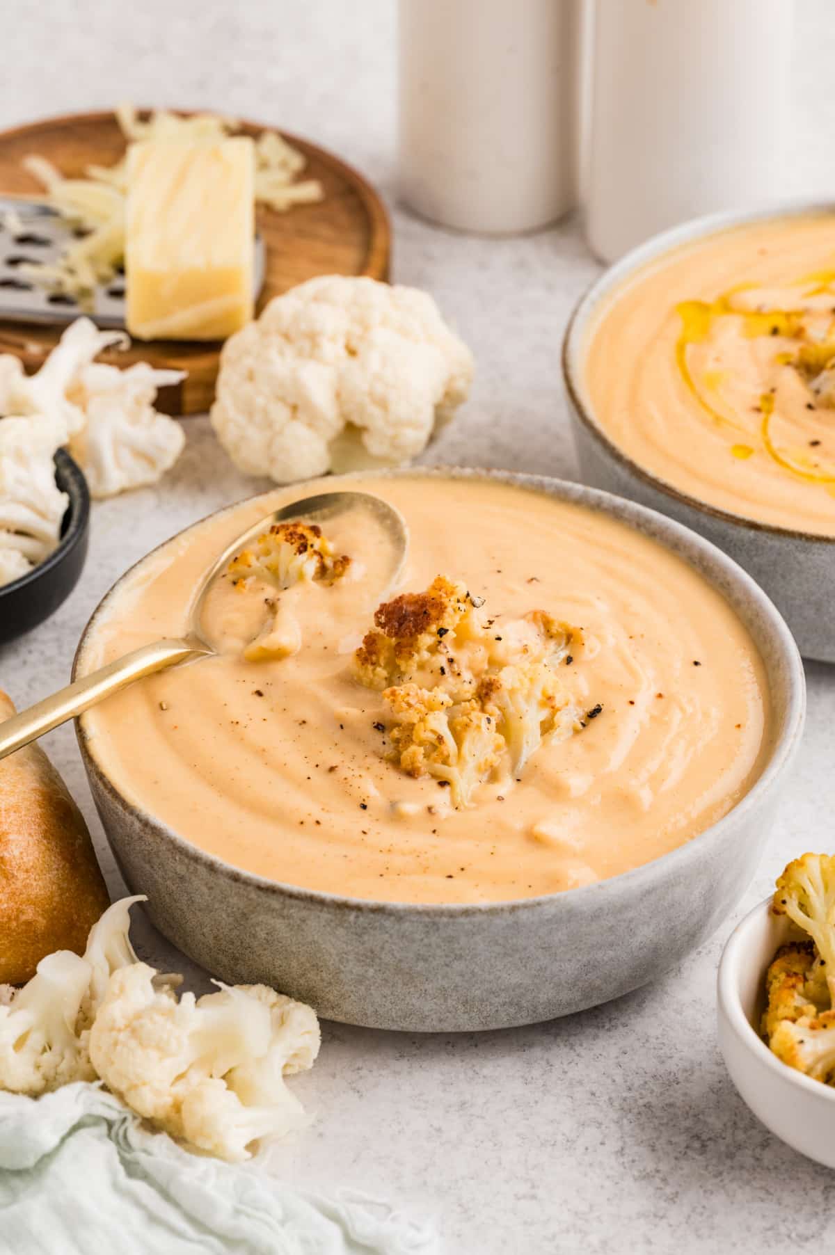 A bowl of creamy cauliflower soup garnished with roasted cauliflower florets and cracked black pepper, ready to serve. Creamy cauliflower soup topped with roasted cauliflower florets, black pepper, and olive oil, served with bread on the side.