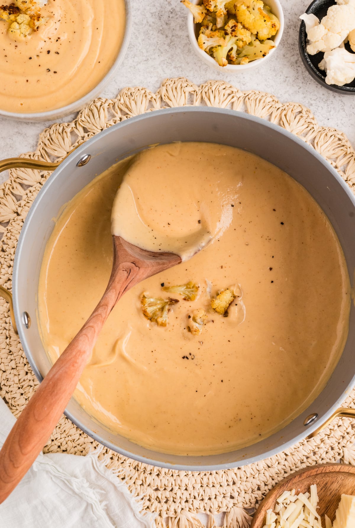 Roasted Cauliflower Soup gently stirred in a wide pot with a wooden spoon and topped with reserved roasted cauliflower. Roasted Cauliflower Soup being stirred in a pot with a wooden spoon and finished with roasted cauliflower florets.