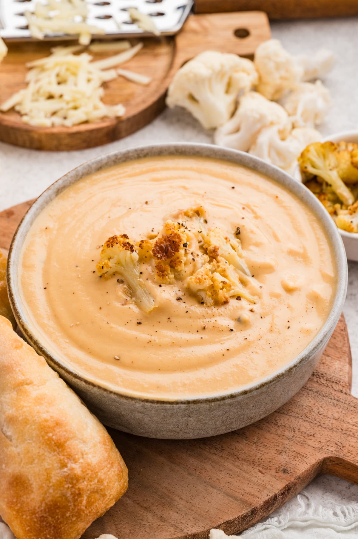 A bowl of Roasted Cauliflower Soup finished with reserved roasted florets and freshly cracked black pepper, Roasted Cauliflower Soup topped with caramelized cauliflower florets and black pepper, served in a bowl with crusty bread.