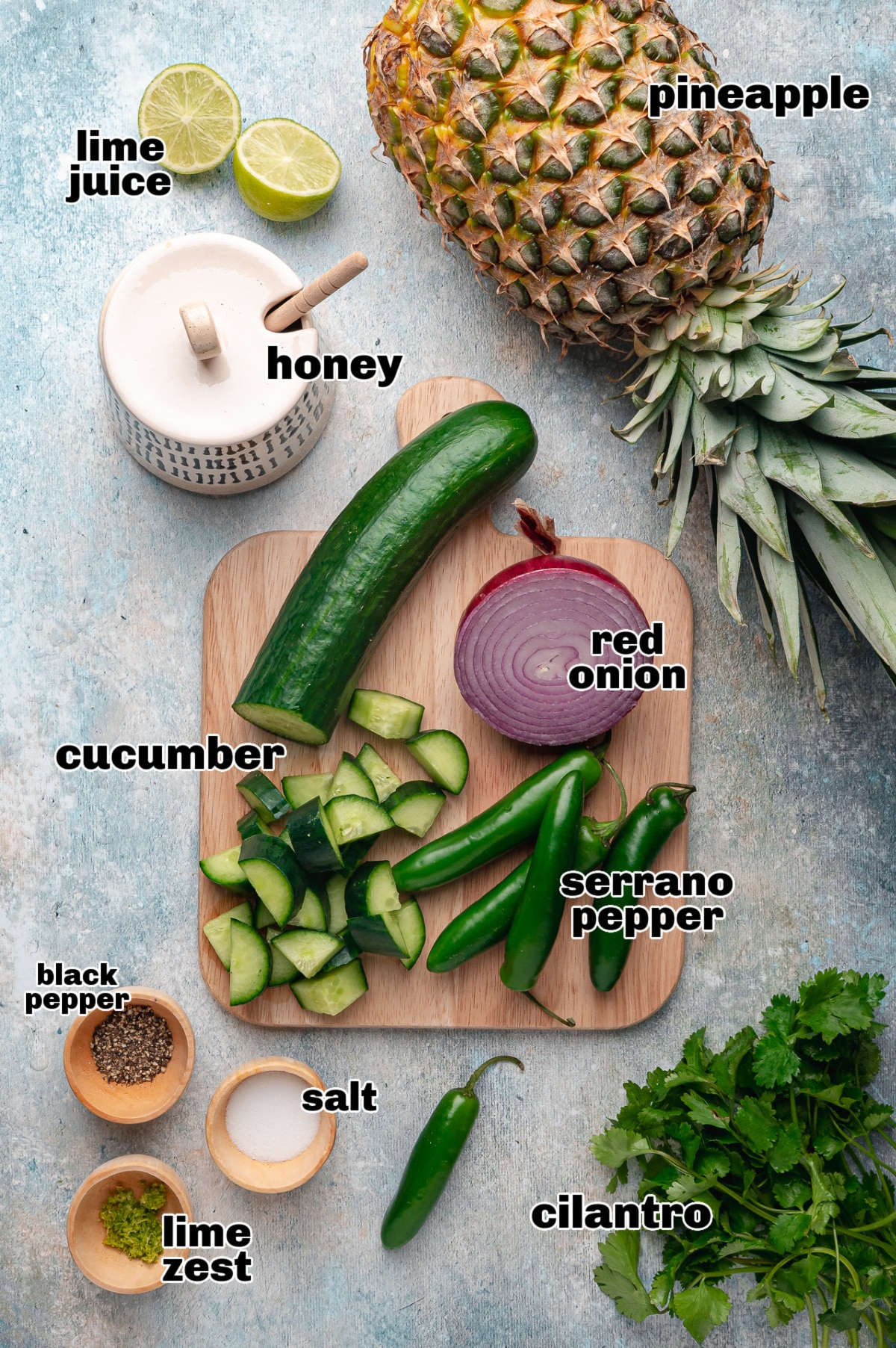 Ingredients for pineapple cucumber salad including fresh pineapple, cucumber, red onion, serrano peppers, lime juice, lime zest, honey, salt, black pepper, and cilantro.