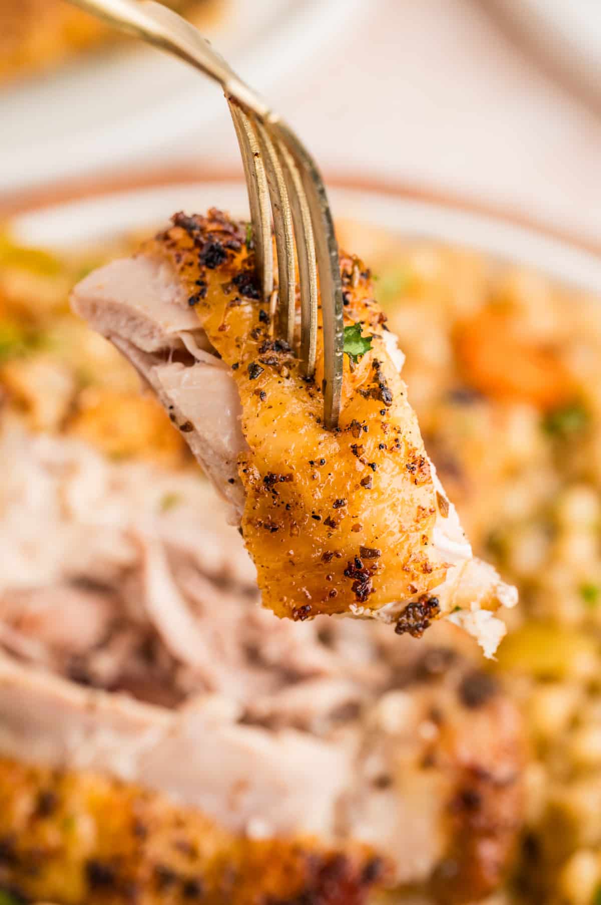 Fork lifting a piece of crispy chicken thigh over pearl couscous, showing golden skin and tender meat.
