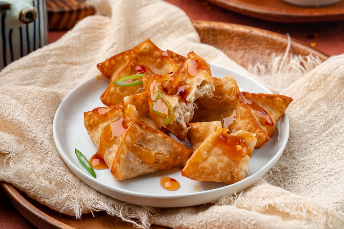 Crab rangoon arranged on a plate, fried until crisp and drizzled with sweet and spicy dipping sauce.