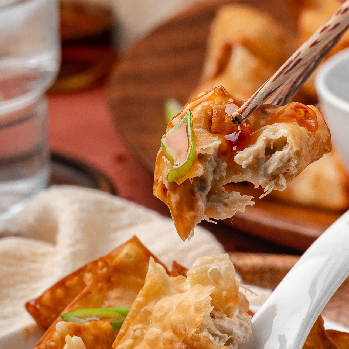 Homemade crab rangoon piled on a serving plate with crisp edges, creamy crab filling, and dipping sauce on the side.