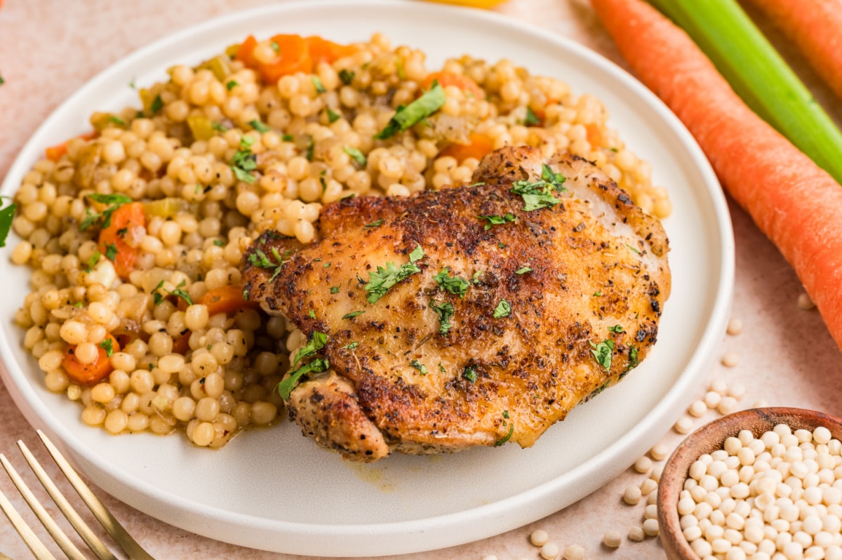 Crispy baked chicken thigh served with pearl couscous and vegetables on a plate.