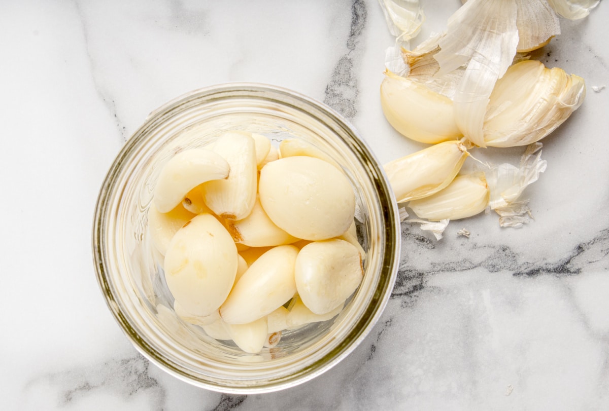 Fresh peeled garlic cloves resting in a mason jar, ready to be covered with raw honey for fermentation. Peeled fresh garlic cloves placed in a wide-mouth mason jar before adding honey for fermentation.