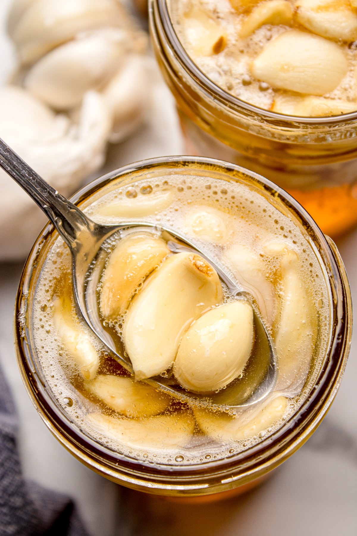 A jar of fermented honey garlic with softened whole garlic cloves resting in raw honey as fermentation begins. Fermented honey garlic with whole garlic cloves submerged in raw honey, showing bubbles from active fermentation.