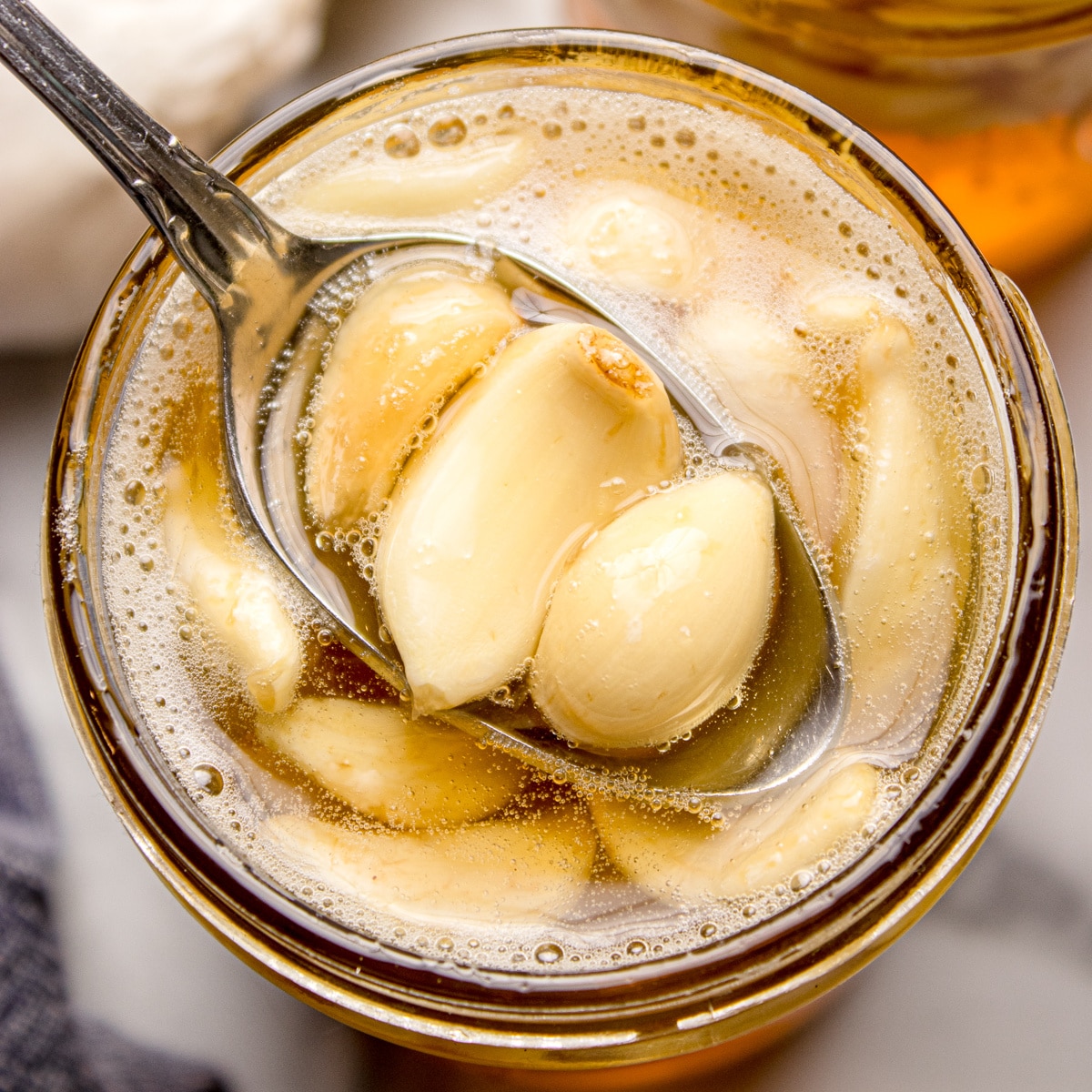 Fermented honey garlic with whole garlic cloves lifted in a spoon, surrounded by lightly bubbling honey inside a glass jar.