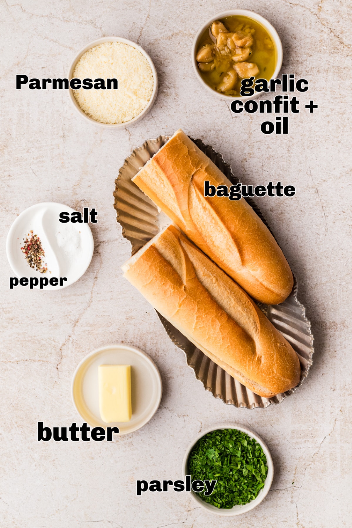 Measured ingredients arranged for making garlic bread with garlic confit and Parmesan Ingredients for air fryer garlic bread including baguette, garlic confit with oil, butter, Parmesan, parsley, salt, and pepper