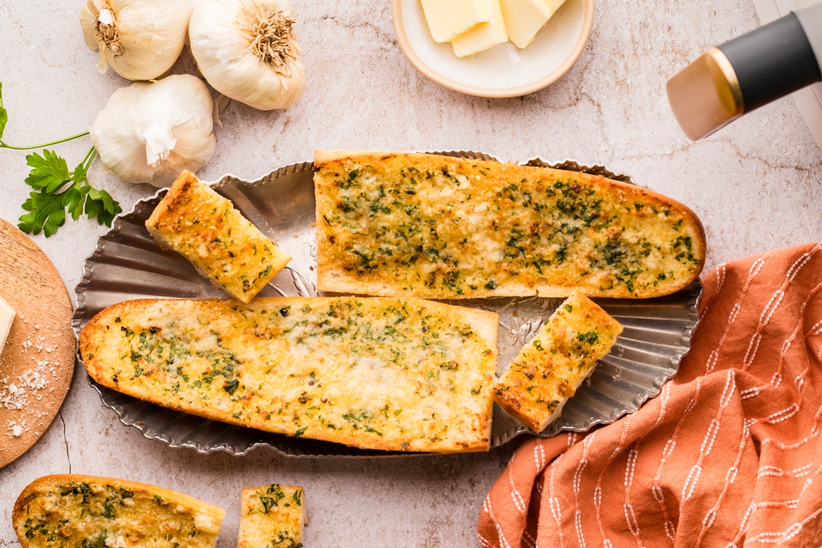 Whole pieces of garlic confit air fryer bread served crisp and golden with herbs and cheese Garlic confit air fryer bread arranged on a platter with golden tops, parsley, and Parmesan