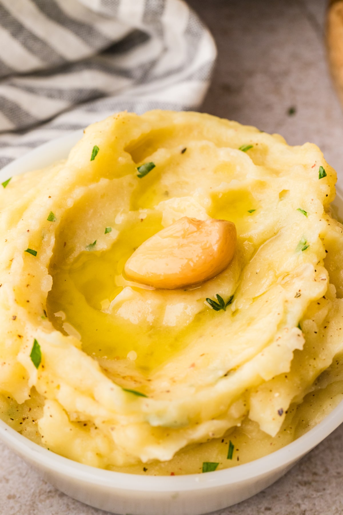 Slow cooker garlic confit mashed potatoes topped with a soft confit garlic clove and olive oil, showing a creamy, smooth texture in a white bowl.