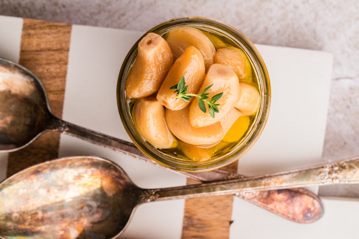 Jar of soft garlic cloves fully submerged in olive oil with thyme.