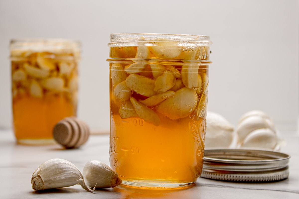 A jar of fermented honey garlic resting at room temperature as the honey loosens and the garlic softens. Fermented honey garlic in a mason jar with whole garlic cloves suspended in honey as fermentation develops.