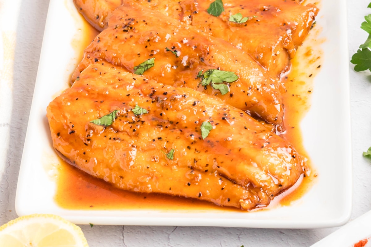 Honey glazed salmon arranged on a white platter with a smooth honey glaze, cracked black pepper, and chopped parsley.