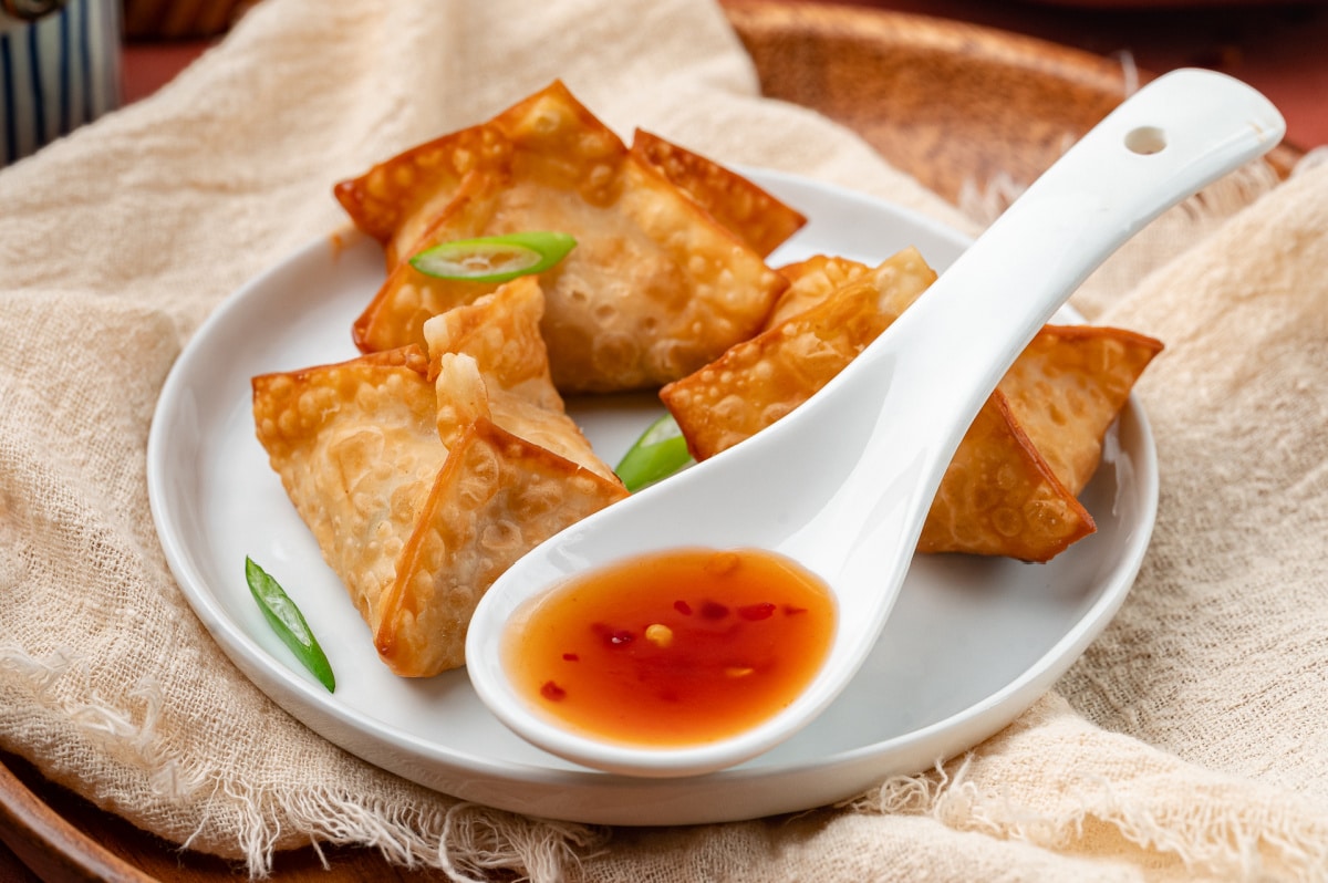 Homemade crab rangoon with crisp wonton wrappers served alongside a sweet and spicy dipping sauce.